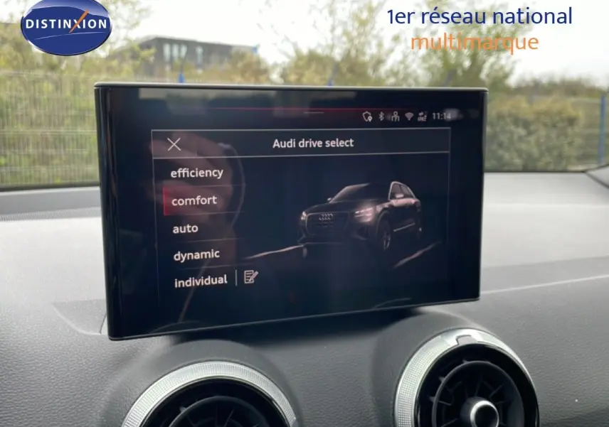 Écran central affichant le menu Audi drive select avec options de conduite, intérieur noir du Q2 visible en arrière-plan.
