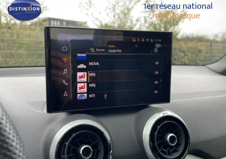 Écran tactile central affichant les radios DAB/FM, avec les aérateurs ronds du tableau de bord d’un Audi Q2 noir Mito Metal.