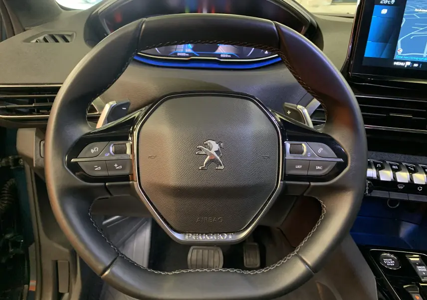Vue rapprochée du volant cuir noir du Peugeot 5008 2024 avec commandes intégrées et tableau de bord numérique.
