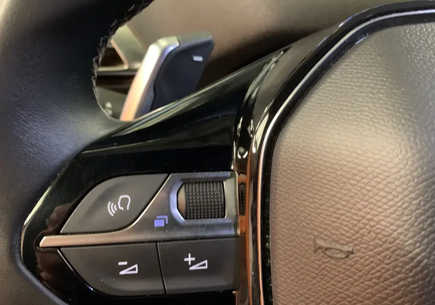 Gros plan sur les commandes gauche du volant noir du Peugeot 5008 Bleu Célèbes, montrant les boutons de volume et de communication.