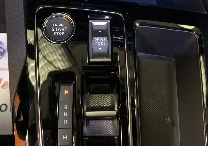 Gros plan sur la console centrale noire brillante du Peugeot 5008 Bleu Célèbes, avec bouton start/stop et sélecteur de mode de conduite.