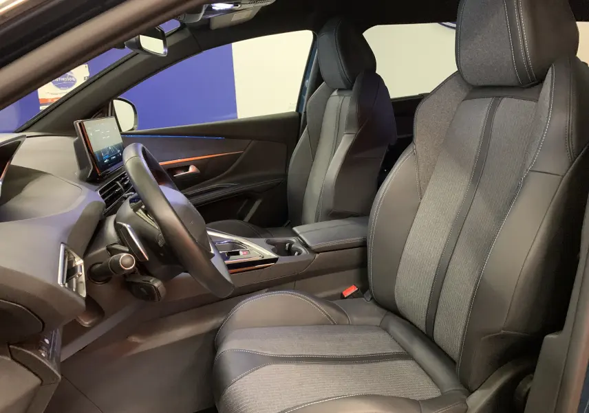 Vue intérieure côté conducteur du Peugeot 5008 2024, sièges en cuir et tissu gris avec tableau de bord moderne.