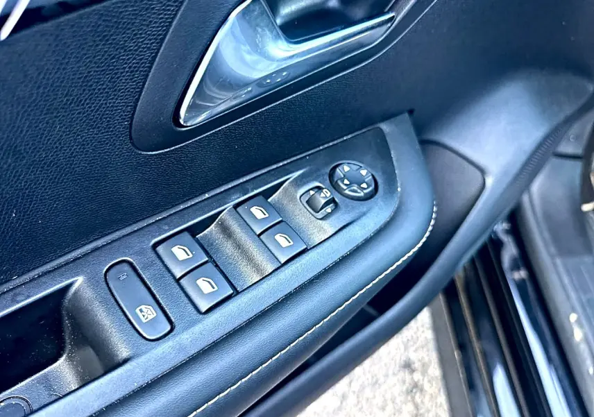 Détail de la porte côté conducteur noire d’une Peugeot 208 1.2 100 allure avec commandes des vitres et rétroviseurs électriques.