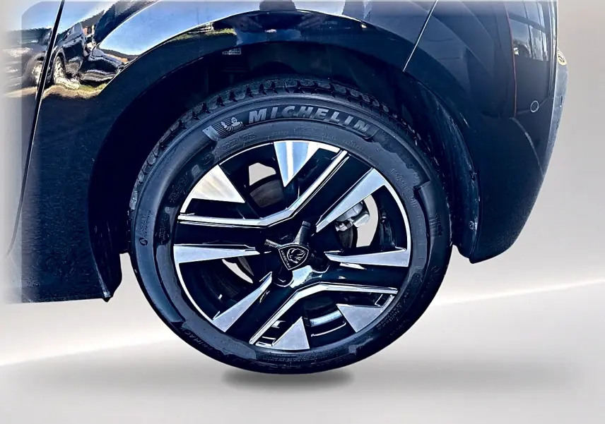 Gros plan sur la roue avant droite noire de la Peugeot 208 1.2 100 allure avec jante alu bicolore et pneu Michelin.