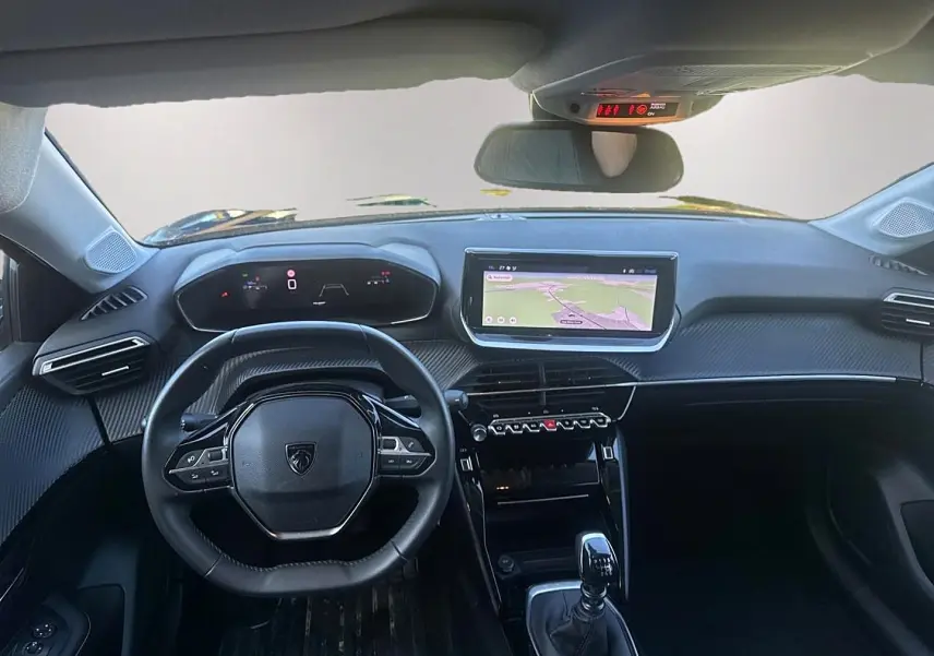 Vue intérieure avant de la Peugeot 208 1.2 100 allure noire, volant compact et écran tactile central avec navigation affichée.