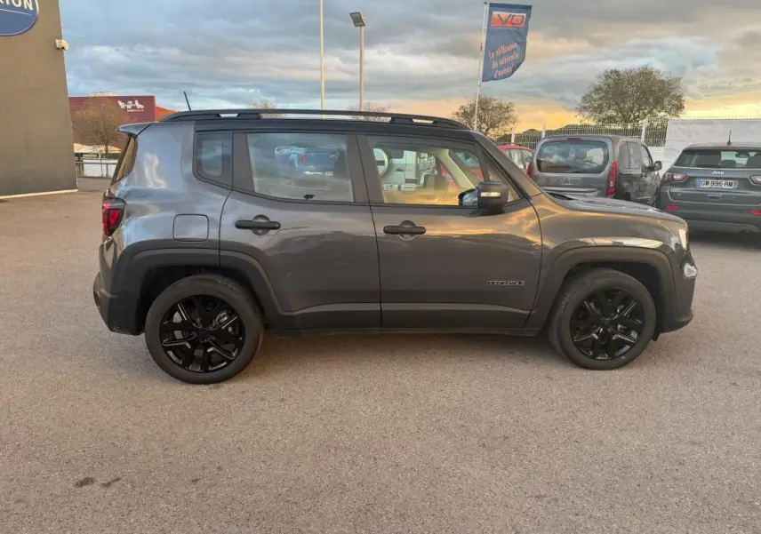 Profil côté gauche d'un Jeep Renegade gris anthracite 2024 avec jantes alliage noires et barres de toit visibles.