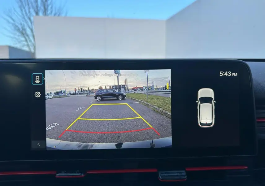 Rétroviseur droit noir brillant du Hyundai Kona II 1.6 Hybrid 138 N Line en Ecotronic Grey, reflet du ciel nuageux visible.