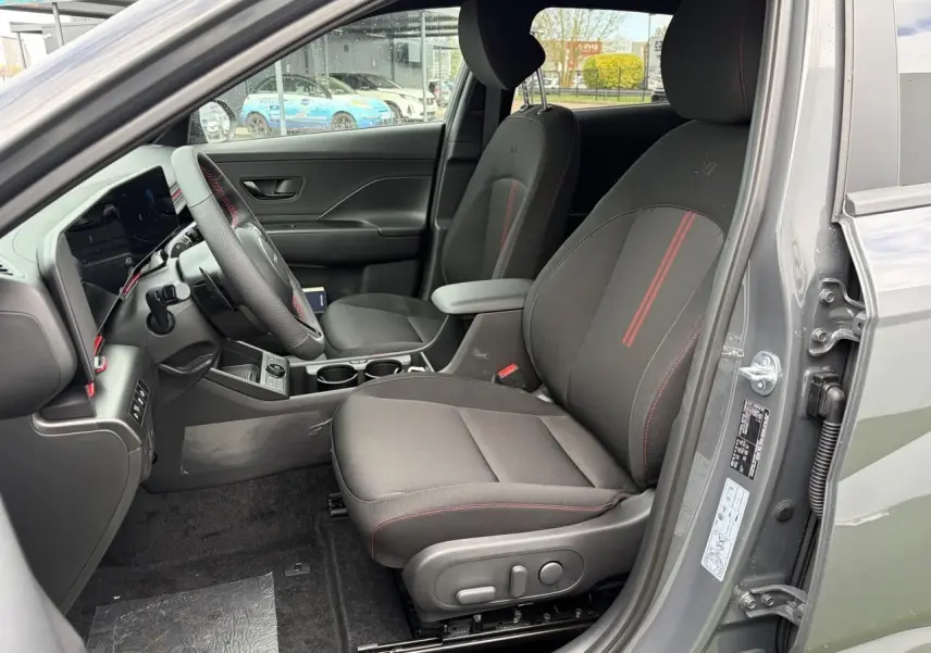 Vue intérieure côté conducteur du Hyundai Kona II 1.6 Hybrid N Line gris Ecotronic avec sièges noirs à surpiqûres rouges.