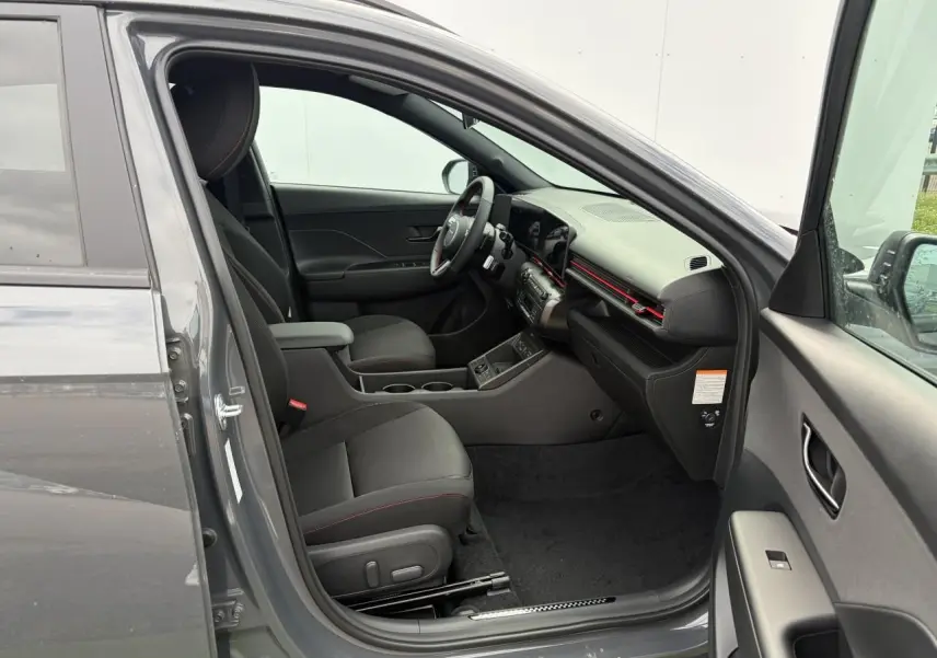Intérieur côté conducteur du Hyundai Kona 2026 gris Ecotronic, avec sièges noirs et détails rouges sur tableau de bord.