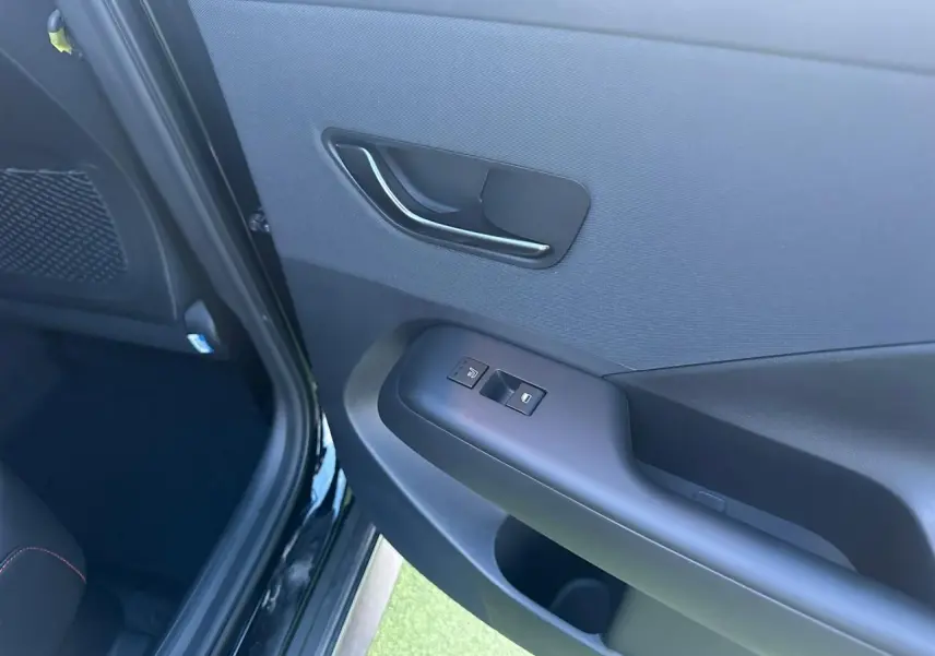 Vue intérieure côté gauche de la porte arrière d'une Hyundai Kona II grise, avec commandes de fenêtre et poignée noire.