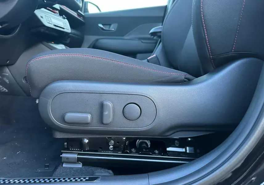 Gros plan sur le siège conducteur noir avec surpiqûres rouges et commandes électriques côté gauche du Hyundai KONA 2026.