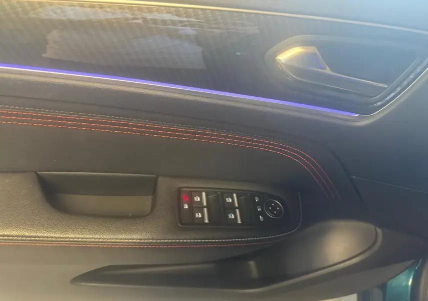 Gros plan sur la porte côté conducteur du Renault Arkana bleu, avec surpiqûres rouges et commandes de vitres.