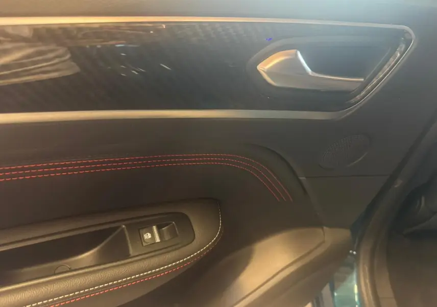 Détail de la porte intérieure côté gauche du Renault Arkana bleu, avec surpiqûres rouges et poignée argentée.