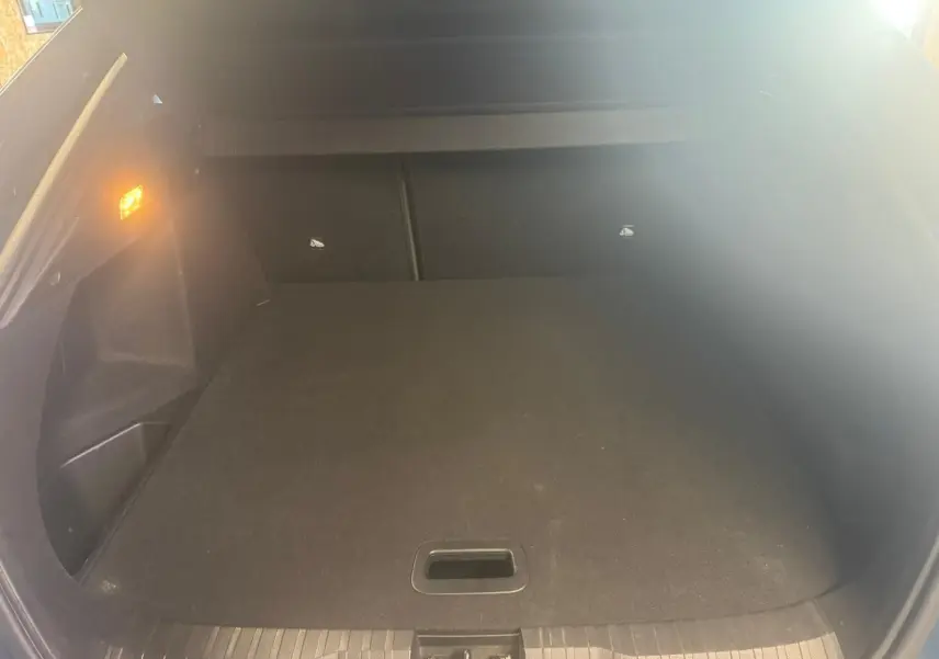 Coffre ouvert vu de l'arrière d'un Renault Arkana bleu, espace de chargement propre et éclairage latéral allumé.
