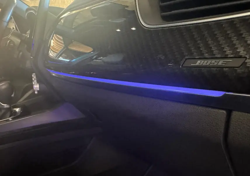 Vue intérieure côté passager du tableau de bord noir avec éclairage d'ambiance bleu et logo Bose sur Renault Arkana 1.3 TCE 140 RS-Line.