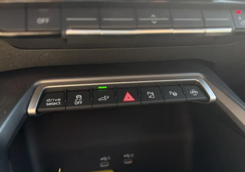 Gros plan sur la rangée de boutons de commande du tableau de bord de l’Audi A3 Sportback noir, avec éclairage vert sur le mode EV.