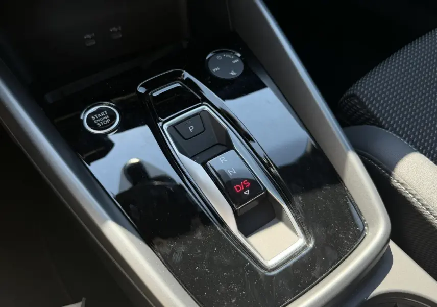 Gros plan sur la console centrale noire brillante de l'Audi A3 Sportback 2025 avec levier de vitesses automatique et bouton start/stop.