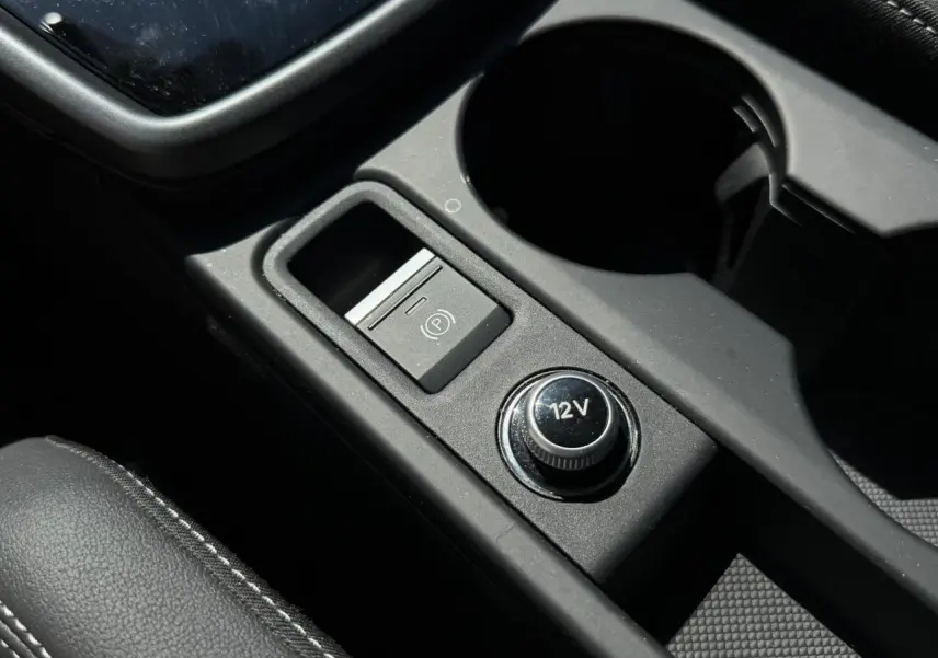 Gros plan sur la console centrale noire de l’Audi A3 Sportback 2025, avec bouton 12V et frein à main électrique.