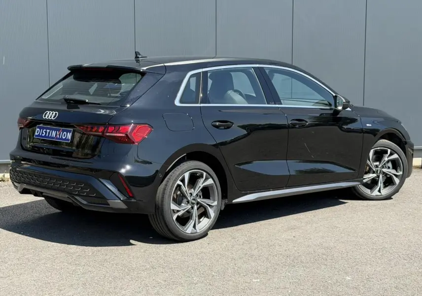 Audi A3 Sportback noir Mythe vue 3/4 arrière droit, avec jantes alliage 5 branches en Y et détails S-Line visibles.