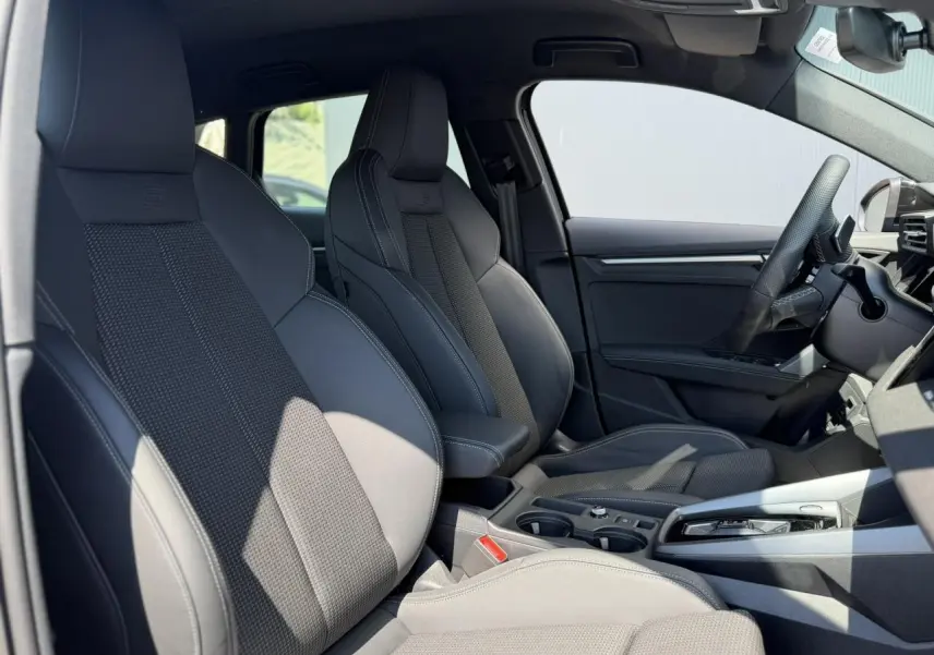 Vue intérieure côté gauche de l'Audi A3 Sportback 2025 avec sièges sport noirs et console centrale élégante.