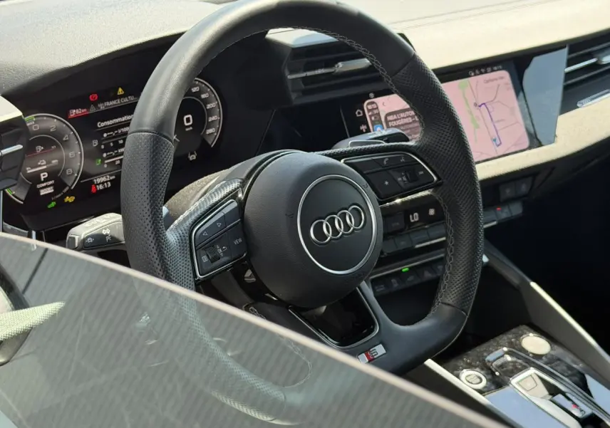 Vue rapprochée du volant sport en cuir perforé avec logo Audi S, tableau de bord numérique et écran central tactile.