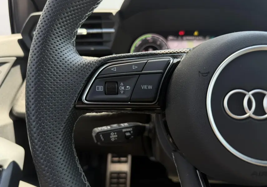 Gros plan sur le volant perforé noir de l'Audi A3 Sportback 2025 avec commandes multifonctions et logo Audi central.