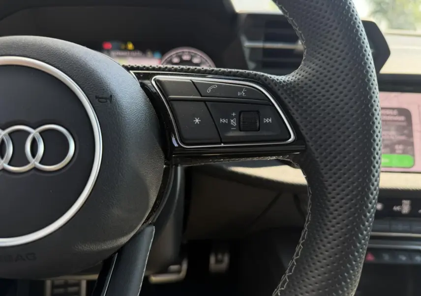 Gros plan sur la partie droite du volant cuir perforé noir de l'Audi A3 Sportback 2025 avec commandes intégrées.