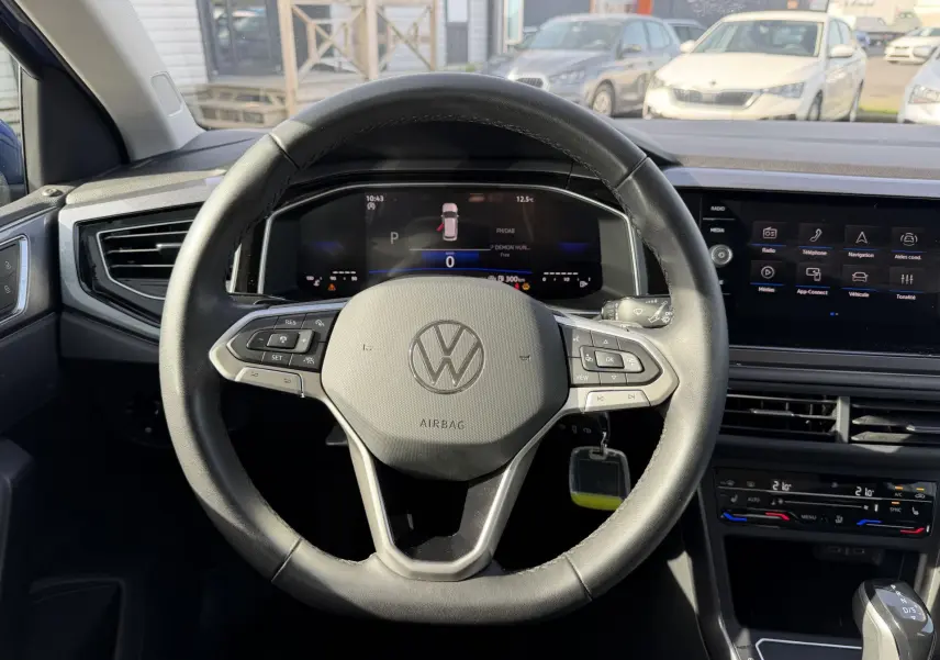 Vue intérieure centrée sur le volant cuir multifonctions d'une Volkswagen Polo bleue avec tableau de bord digital et écran tactile.