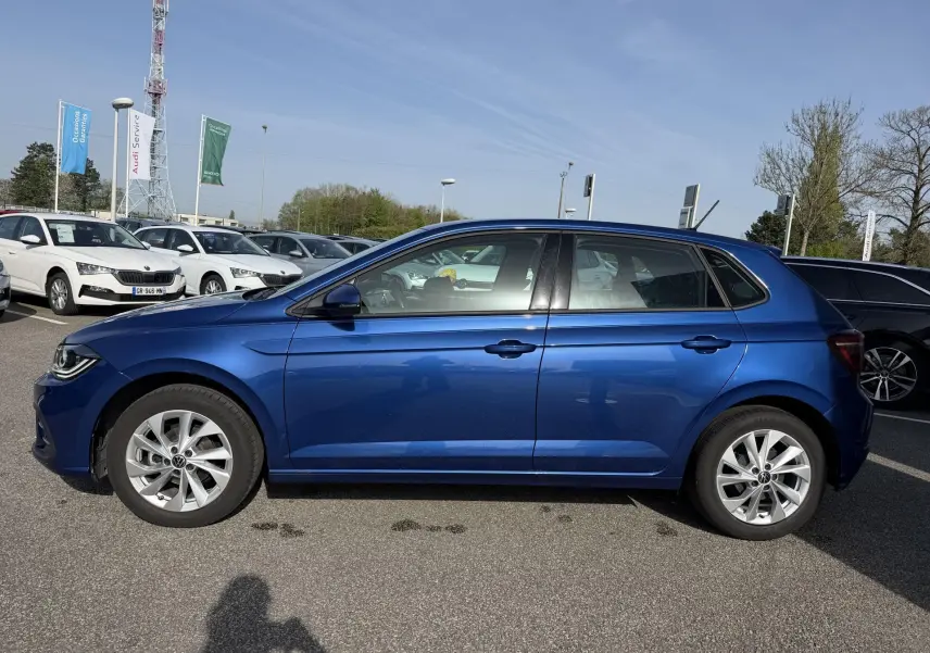 Vue de profil côté gauche d'une Volkswagen Polo 2025 bleu récif métallisé avec jantes alliage 16 pouces sur parking extérieur.