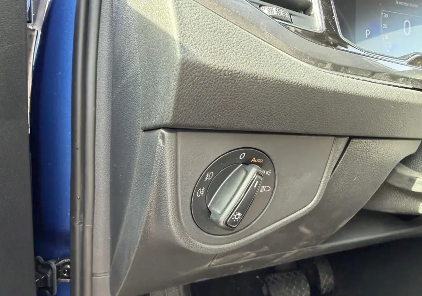 Gros plan sur le bouton de commande des phares côté gauche du tableau de bord d'une Volkswagen Polo bleue 2025.