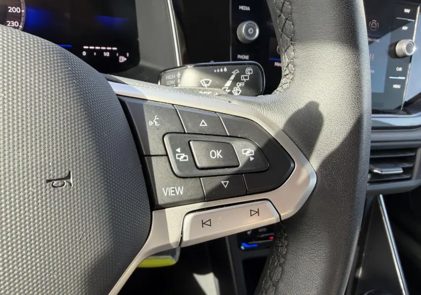 Gros plan sur le volant cuir noir de la Volkswagen Polo 2025, avec commandes multifonctions et écran tactile en arrière-plan.