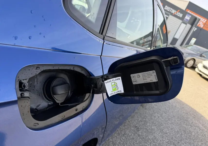 Vue rapprochée du volet de remplissage carburant ouvert côté gauche d'une Volkswagen Polo bleue métallisée.