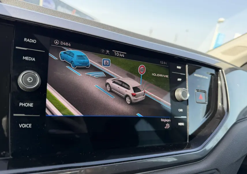 Écran tactile du tableau de bord montrant la caméra de recul avec vue arrière d'une Volkswagen Polo bleue en stationnement.