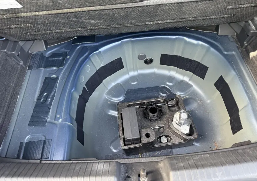 Vue plongeante sur le coffre ouvert d'une Volkswagen Polo bleue, montrant la roue de secours et les outils de bord.
