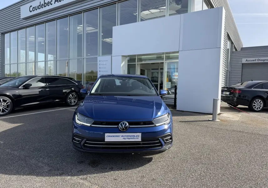 Vue avant d'une Volkswagen Polo bleu récif métallisé garée devant un showroom avec calandre et logo VW visibles.