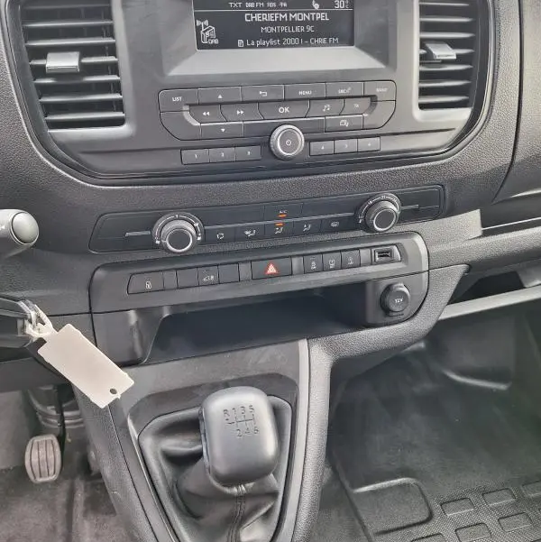 Vue rapprochée de la console centrale noire de l’Opel Vivaro 2025 avec boîte manuelle et écran radio affichant une station FM.