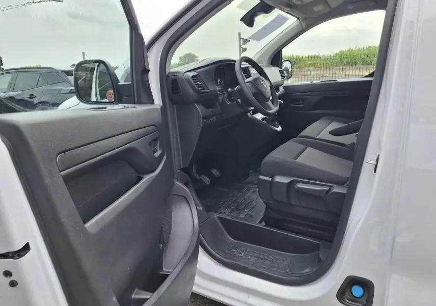 Vue intérieure côté conducteur de l'Opel Vivaro blanc 2025, montrant le tableau de bord et les sièges avant en tissu noir.