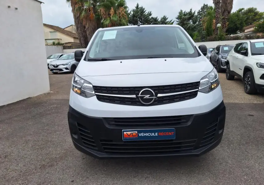 Vue frontale d’un Opel Vivaro blanc 2025 avec calandre noire et pare-chocs avant noir mat, en extérieur.