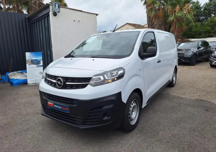 Opel Vivaro blanc en 3/4 avant droit, fourgon utilitaire avec porte latérale et pare-chocs noirs.