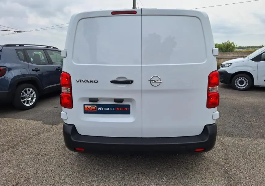 Vue arrière d'un Opel Vivaro blanc avec portes battantes et pare-chocs noir, stationné en extérieur.