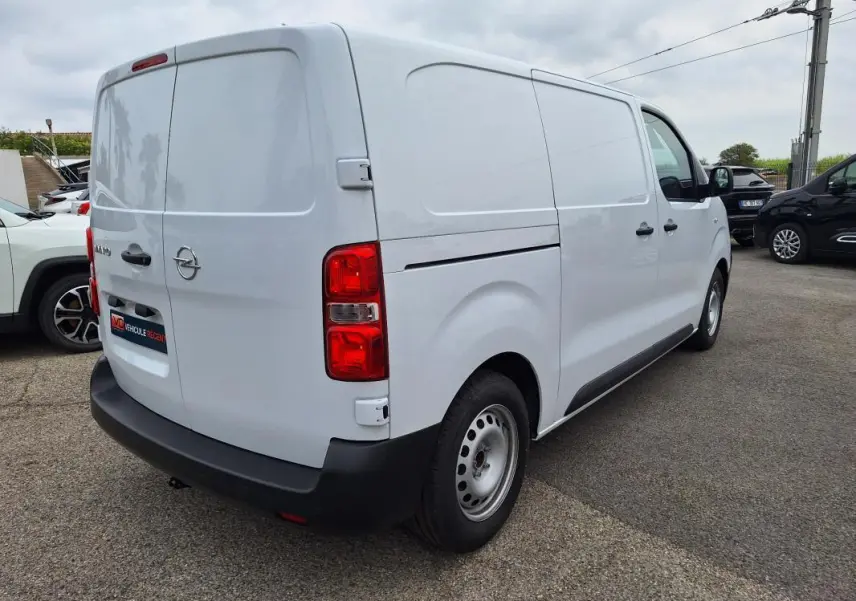 Opel Vivaro blanc vu en 3/4 arrière droit, fourgon avec porte latérale et feux arrière rouges visibles.