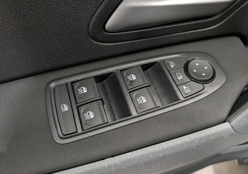 Gros plan sur les commandes de lève-vitres et rétroviseurs côté conducteur du Dacia Duster Hybrid-G blanc Glacier.