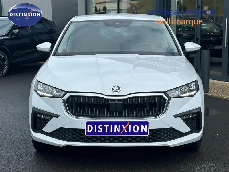 Vue avant d'une Skoda Scala blanche Cristal avec calandre noire et phares LED, stationnée devant un bâtiment.