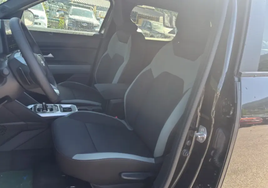 Vue intérieure côté conducteur du Dacia Duster Hybrid-G 150 4x4 noir nacré, mettant en valeur les sièges bicolores et la console centrale.