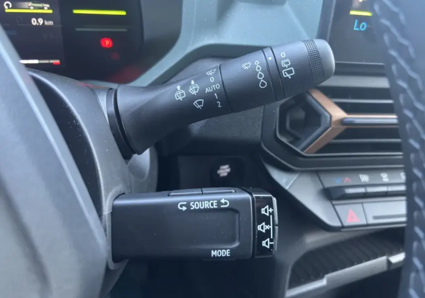 Gros plan sur les commandes au volant du Dacia Duster Hybrid-G 150, avec tableau de bord et aérateurs noirs et bronze visibles.
