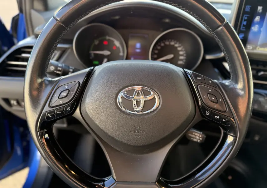 Volant en cuir noir de Toyota C-HR bleu Nebula Metal 2018, avec commandes intégrées et tableau de bord hybride visible.