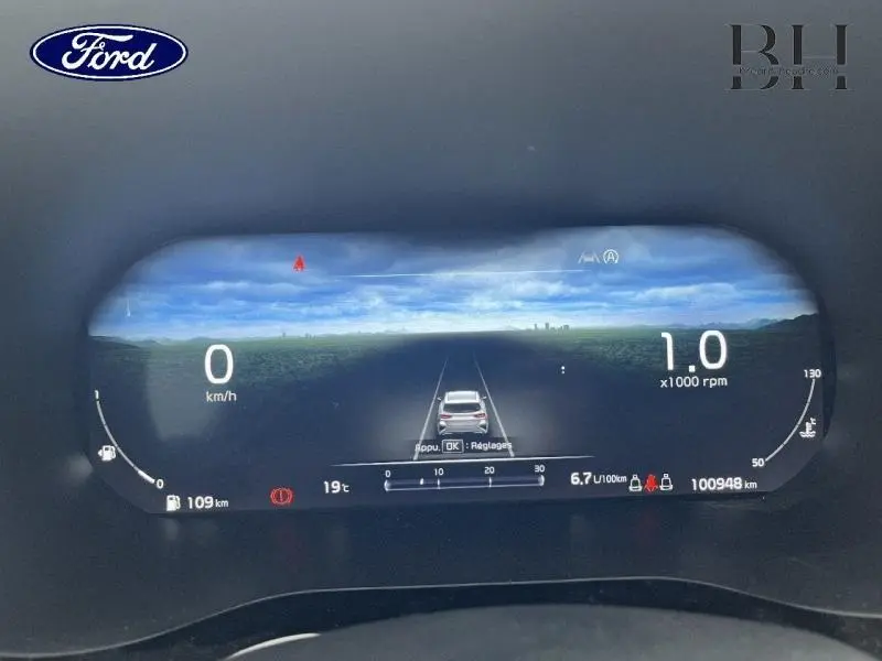 Tableau de bord numérique Ford affichant la vitesse, régime moteur et assistance à la conduite sur fond paysage.