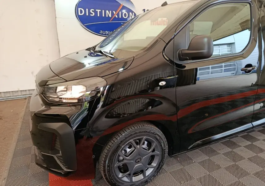 Vue 3/4 avant droit d'un Citroën Jumpy XL noir avec phares allumés et jantes spécifiques en intérieur showroom.