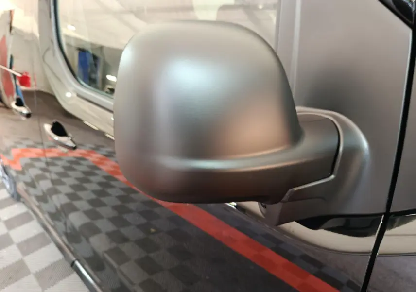 Gros plan sur le rétroviseur côté conducteur du Citroën Jumpy XL noir, reflétant partiellement la porte latérale du véhicule.