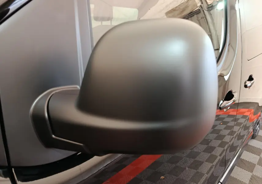 Gros plan sur le rétroviseur côté conducteur du Citroën Jumpy XL noir, avec reflet des poignées de porte et sol damier rouge et noir.